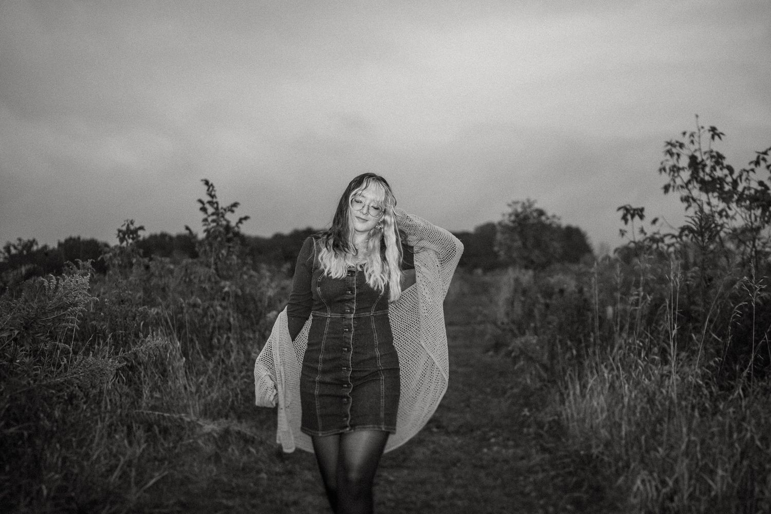Black and white portrait of person in flowing dress standing in natural outdoor setting.