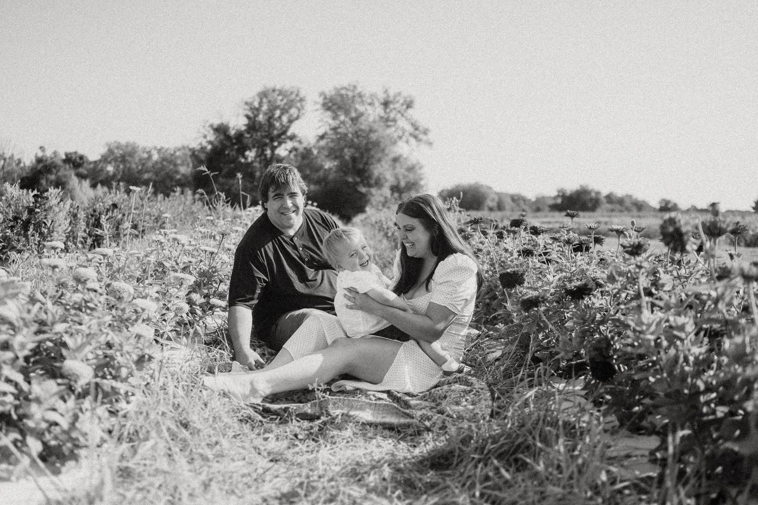 A black and white photograph of a family sharing an intimate moment in a flower field.