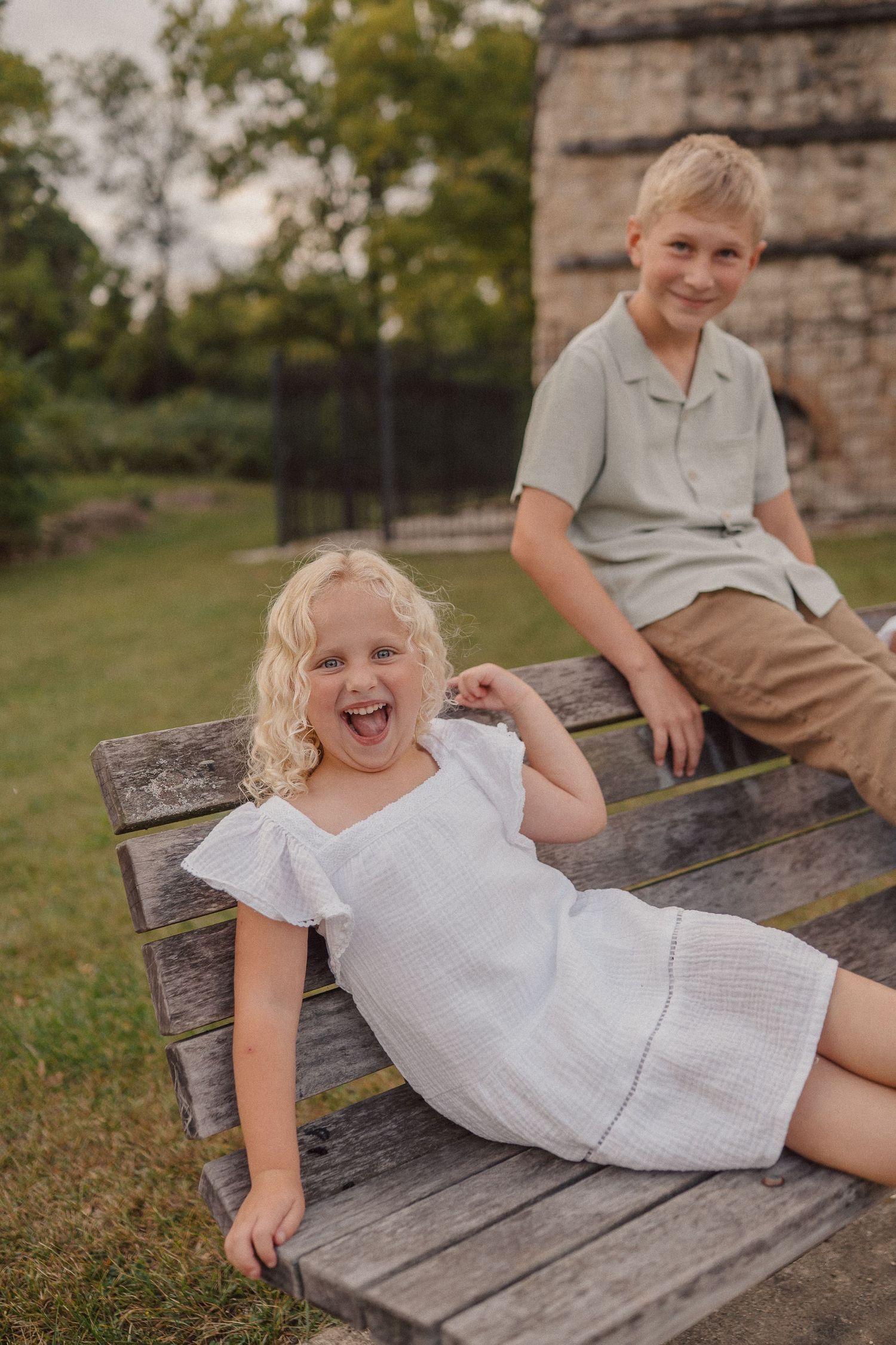 Children lounging and laughing on a rustic wooden bench in an outdoor setting.