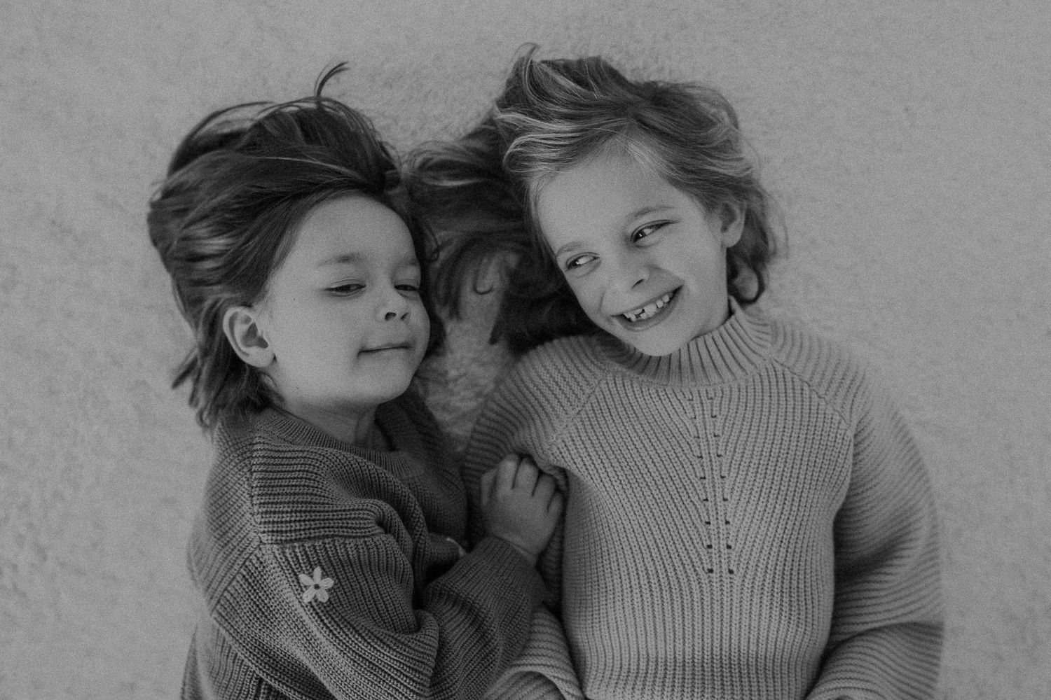Two figures in knit sweaters share a candid black and white moment together.