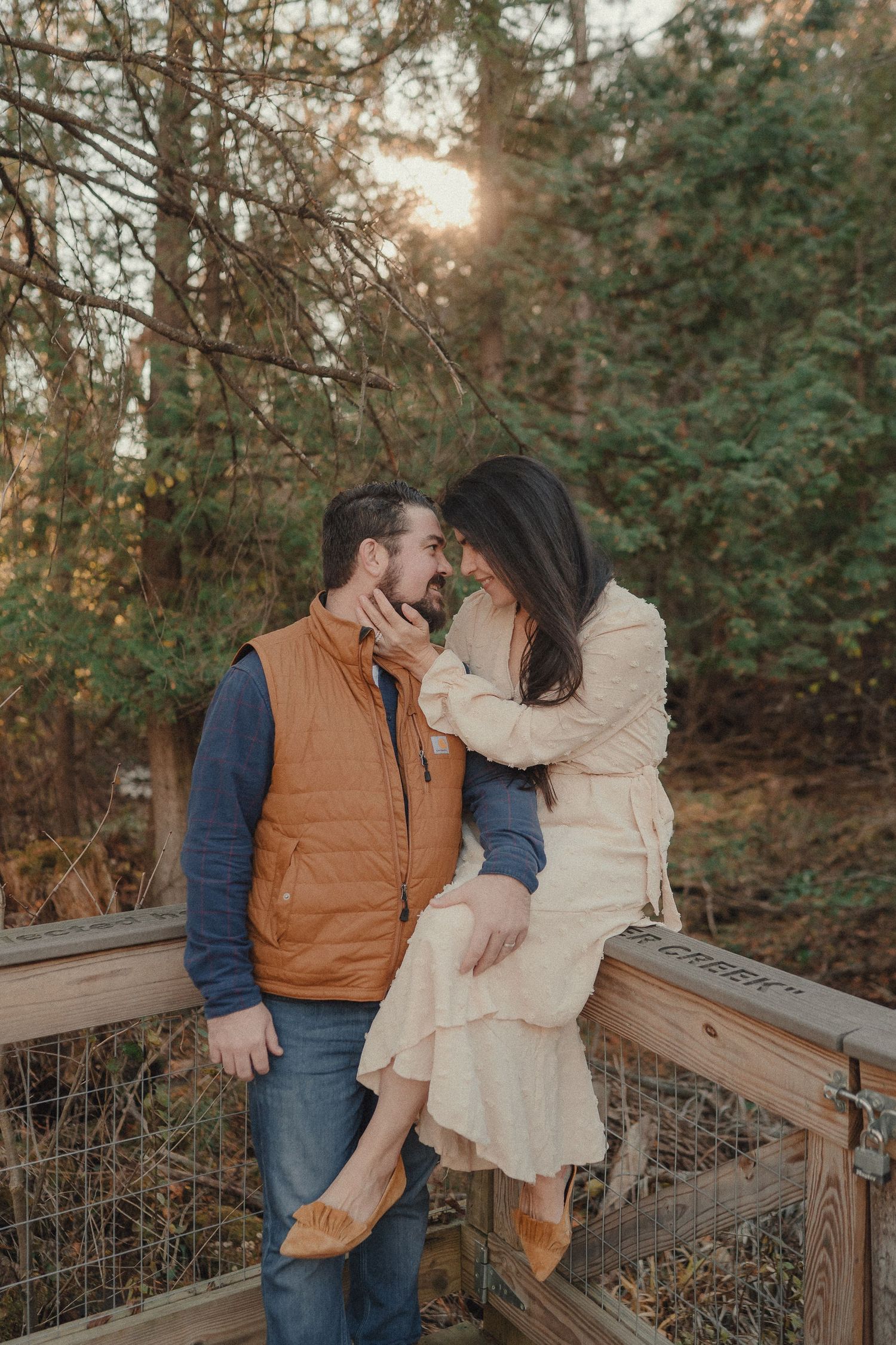 A couple shares a romantic moment on a wooden deck surrounded by trees at sunset.