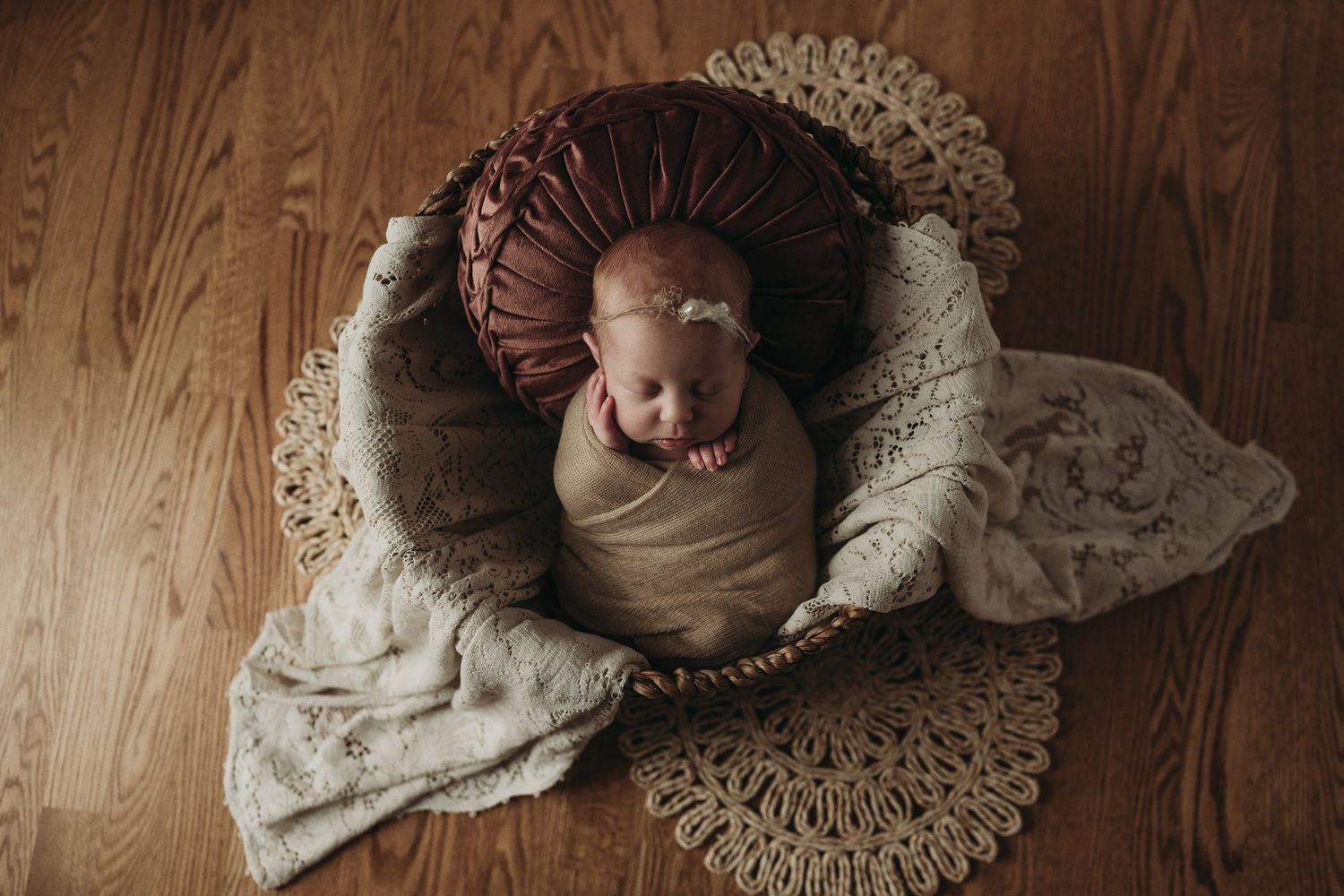 Bird's eye view of sleeping newborn in neutral wrap positioned in round brown cushion.