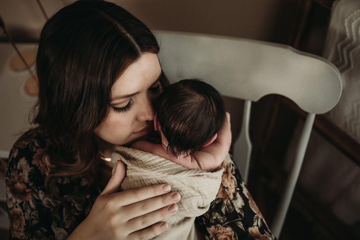 Intimate nursery moment in rocking chair with floral dress and wrapped baby.