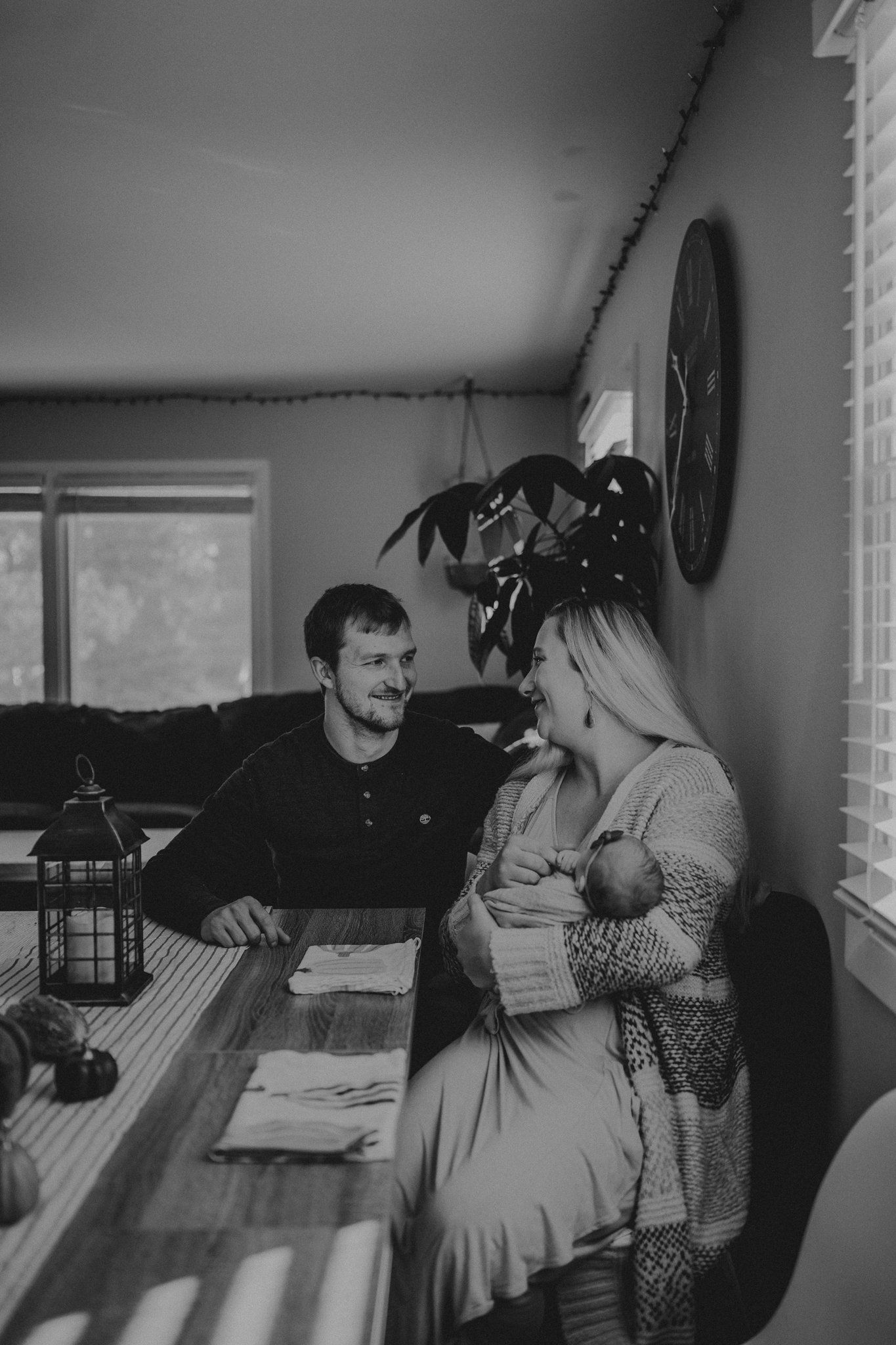 A black and white photo showing a family moment at a dining table with natural window light.