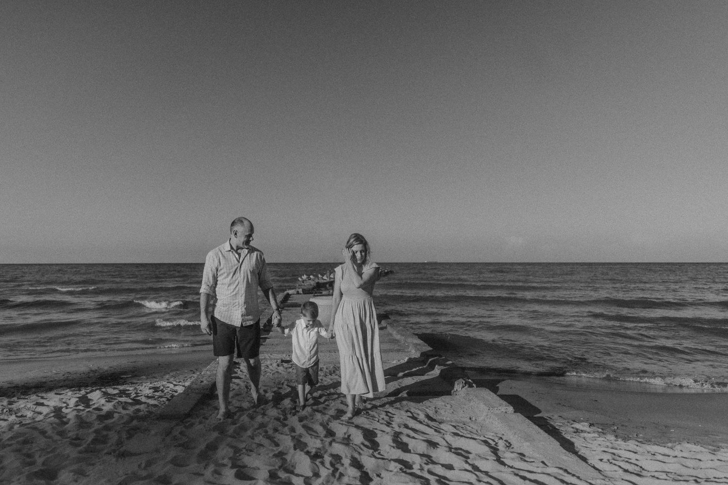 Three people standing together on a beach with waves crashing behind them at sunset.