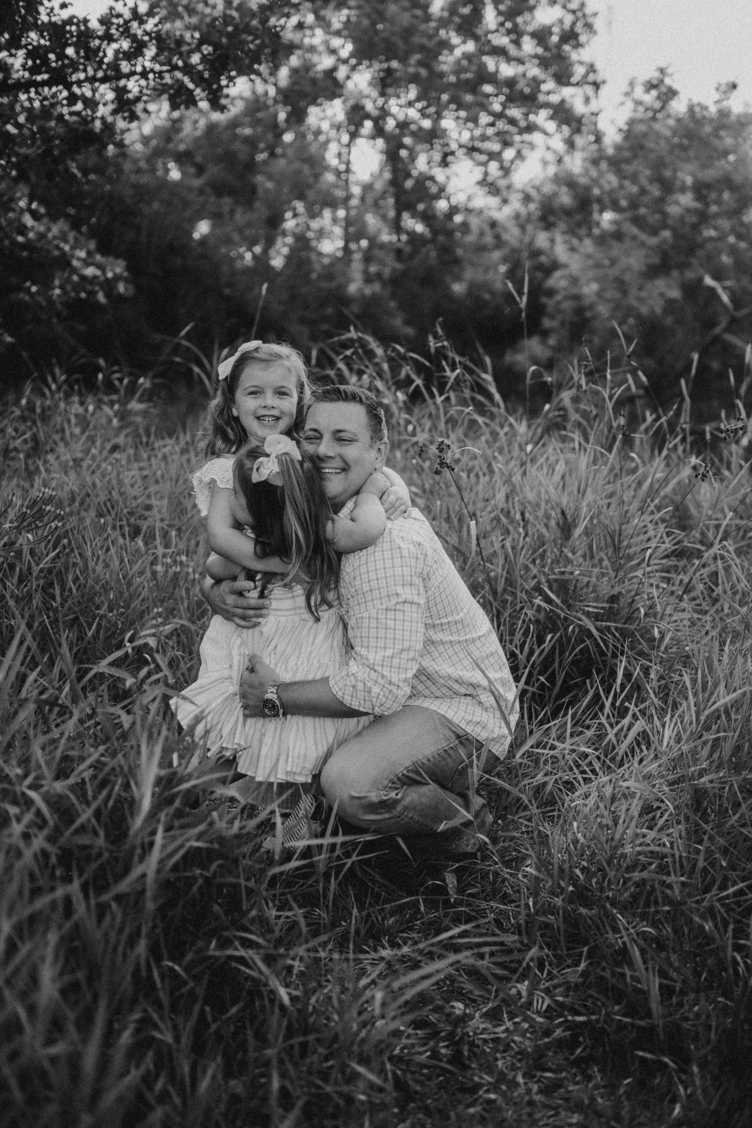 A tender black and white portrait of a warm embrace in tall grass with a natural backdrop.