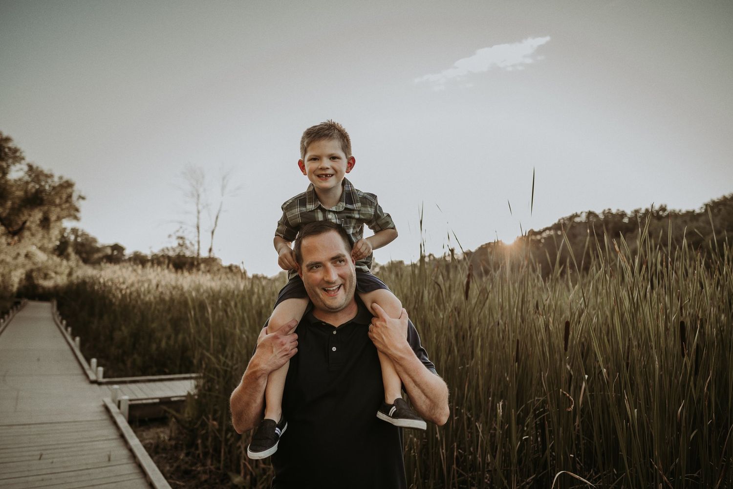 Parent and child enjoying a playful shoulder ride outdoors among tall grass.