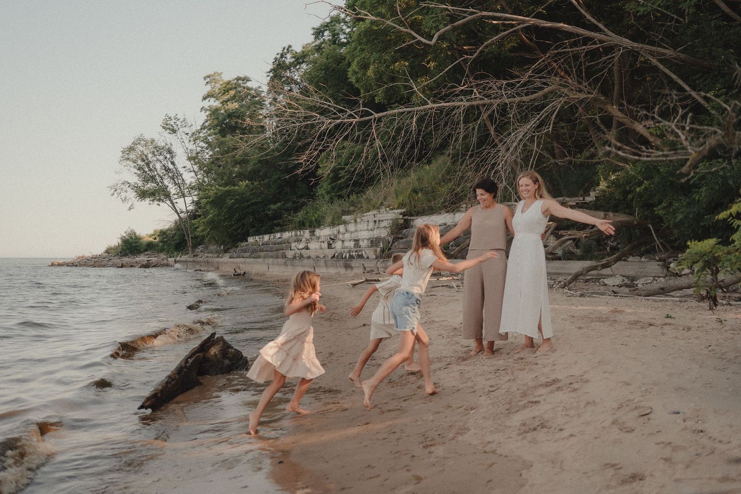A joyful family of four holds hands dancing along a scenic sandy beach at golden hour.