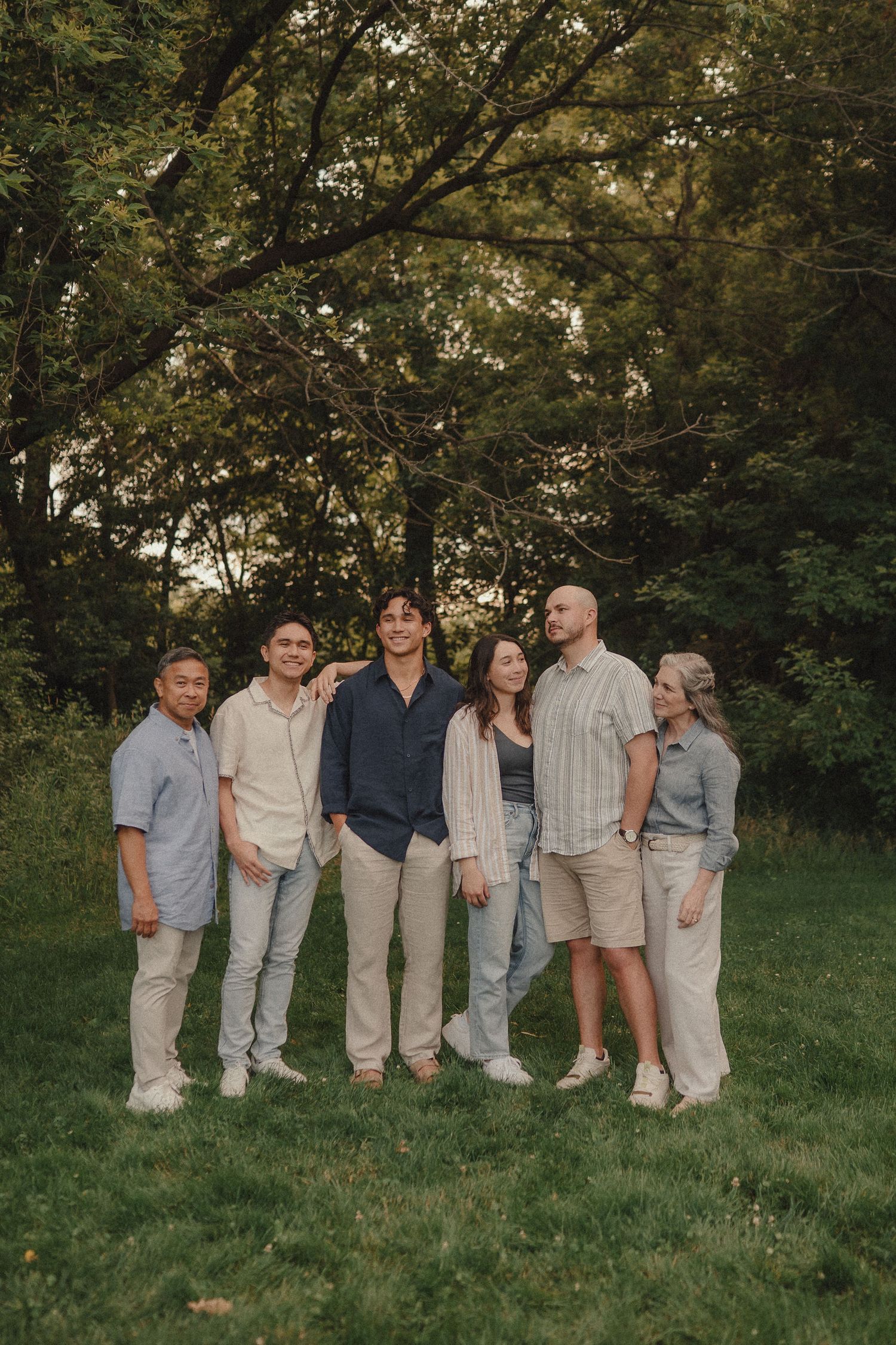 Family of seven posing together on a green lawn surrounded by trees at dusk.