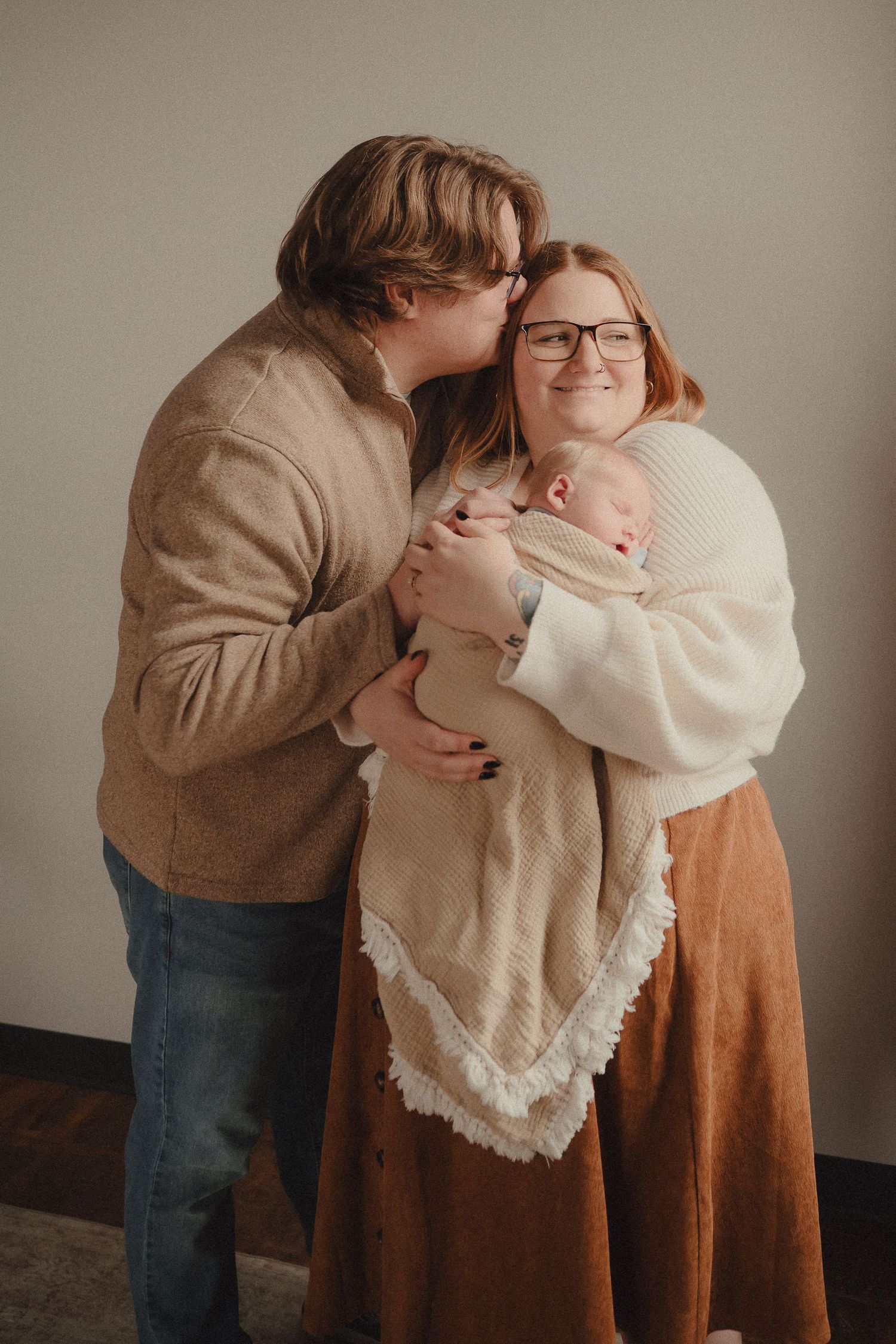 Happy new parents sharing a tender moment, father kissing mother's cheek as she holds their swaddled newborn baby.