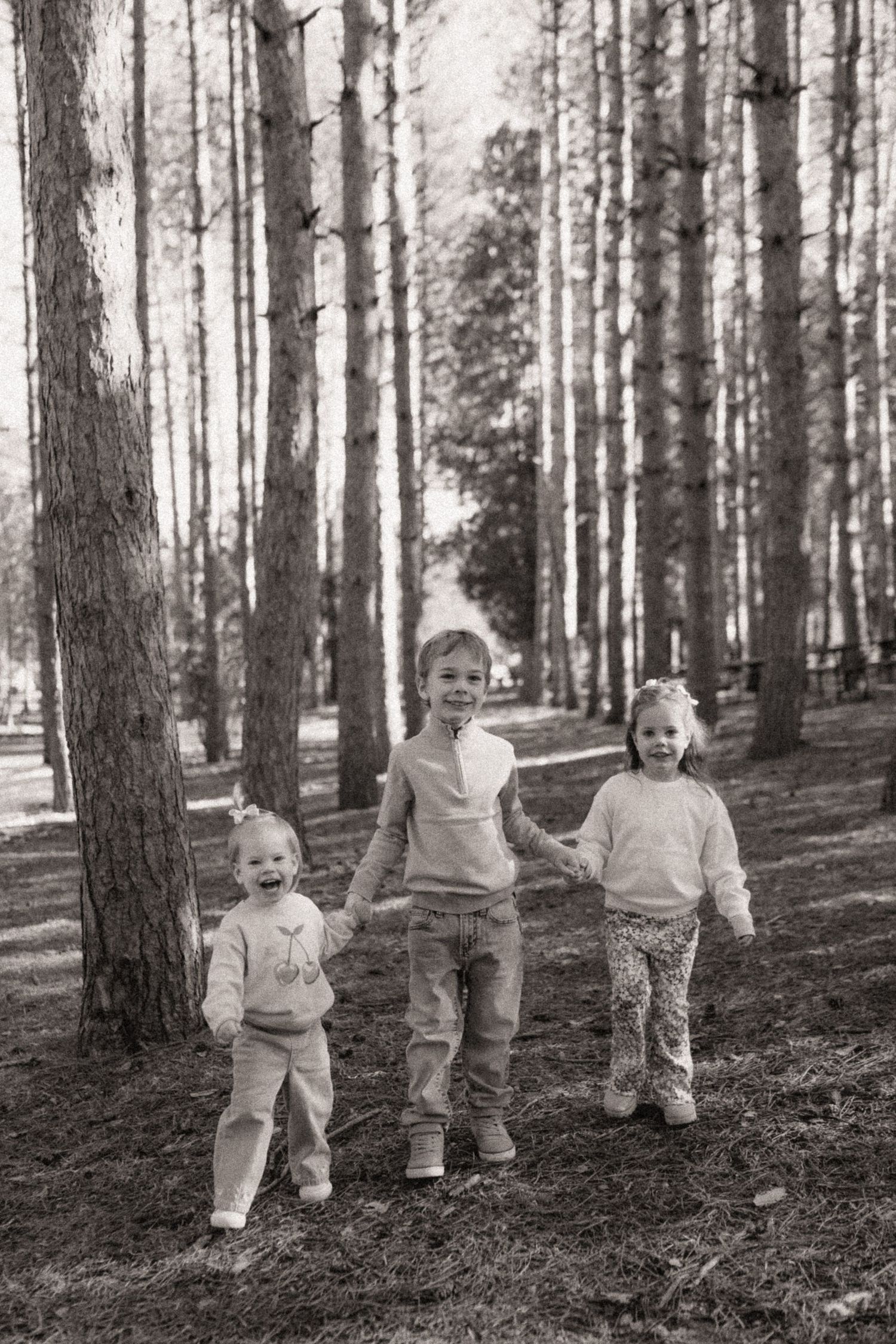 Black and white photo sequence showing small children walking among tall pine trees in a forest.