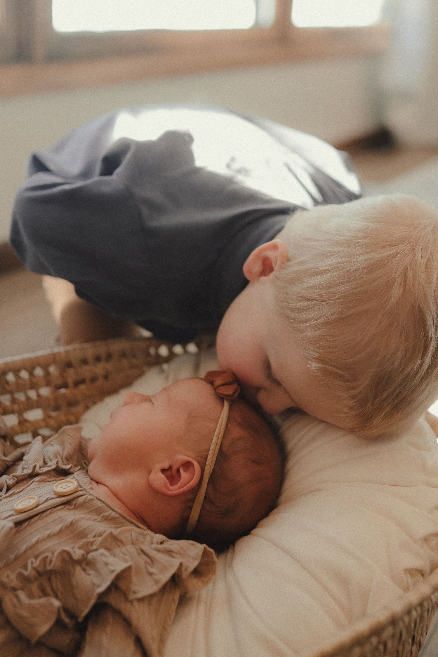 A sleeping baby rests peacefully on soft beige bedding in natural window light.