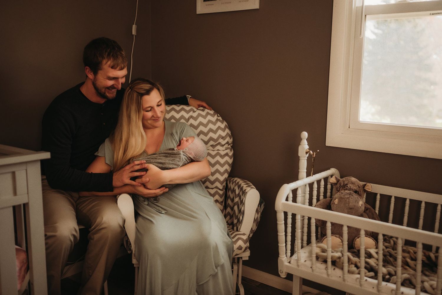 Intimate family moment in nursery rocking chair by window.