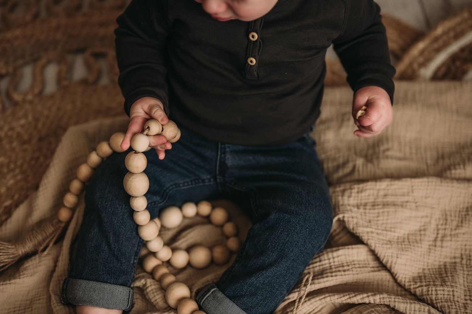 Overhead view of small hands playing with wooden beads on a beige blanket.