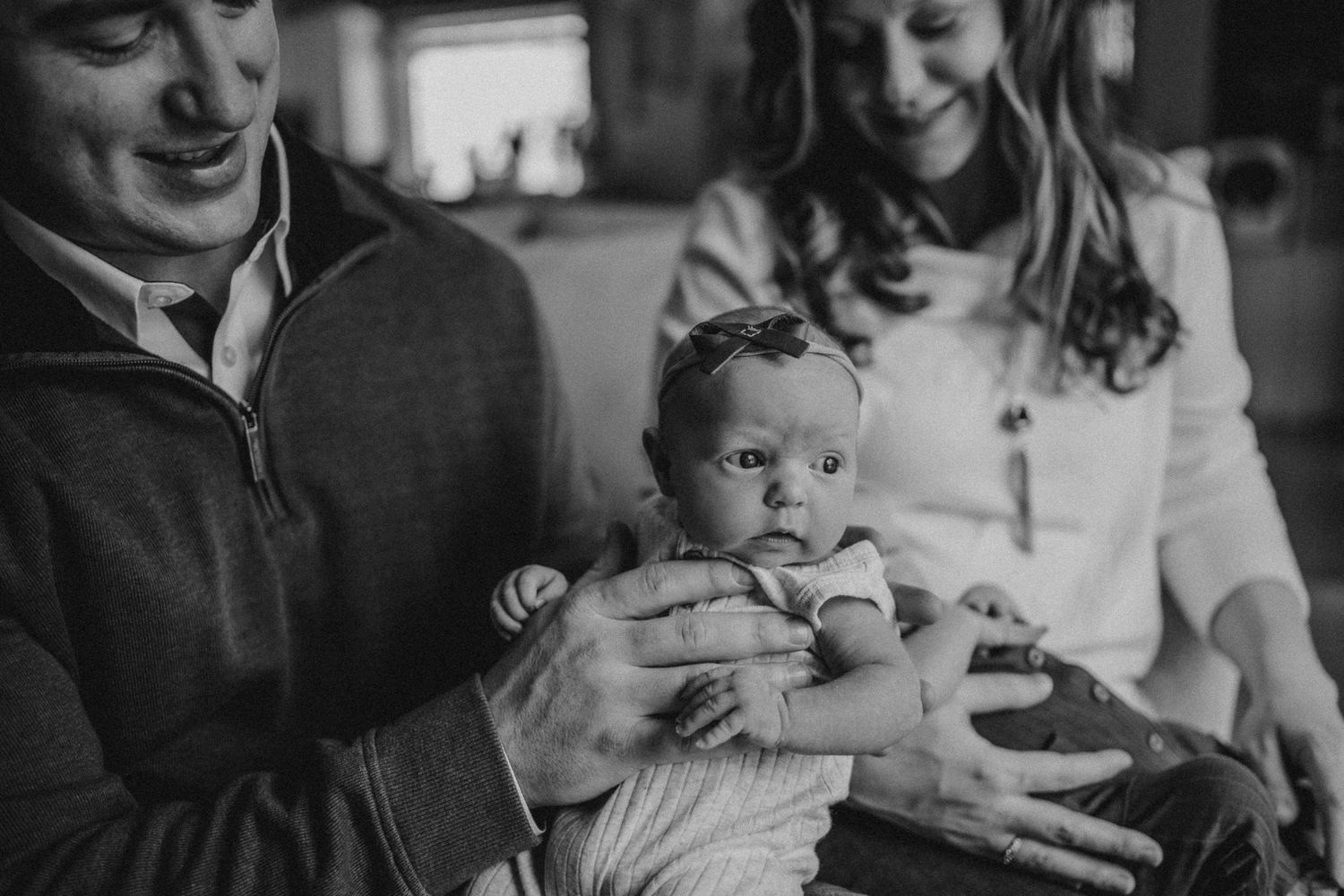 A black and white candid photo of parents with their infant on a couch.