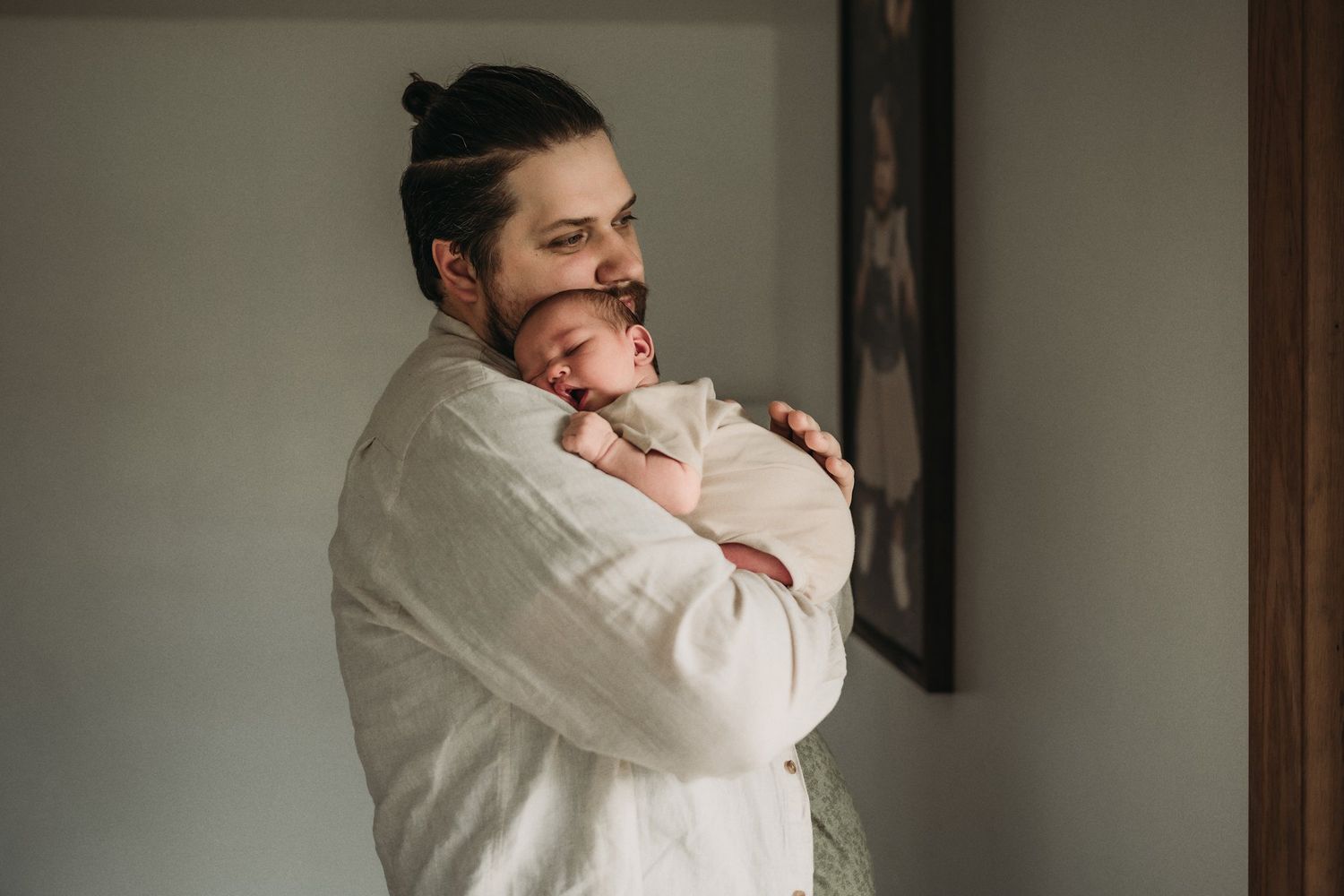 A tender moment captured as someone in a white shirt cradles a newborn baby against their chest.