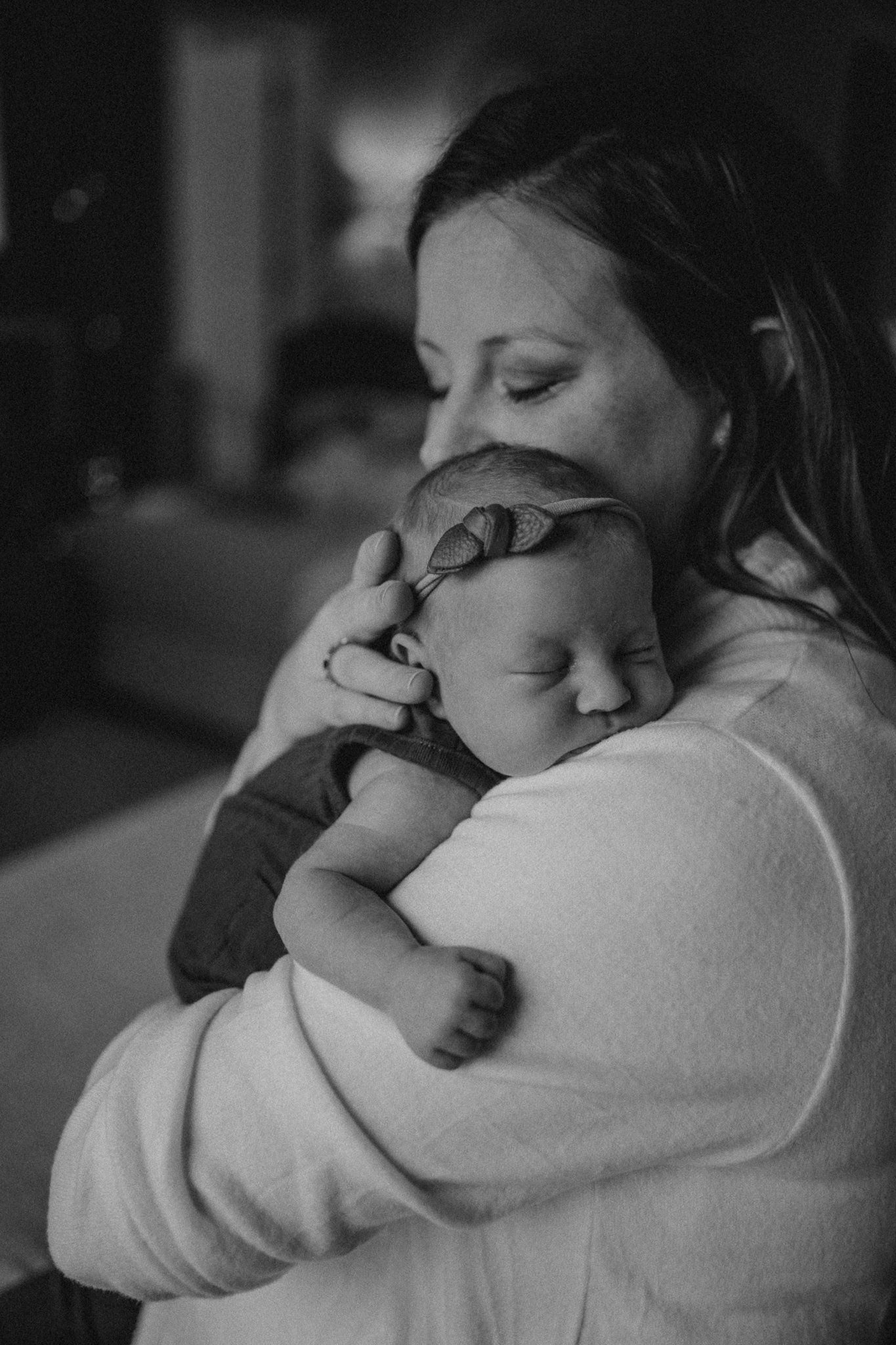 A tender black and white portrait of a parent cradling a sleeping newborn baby against their chest.