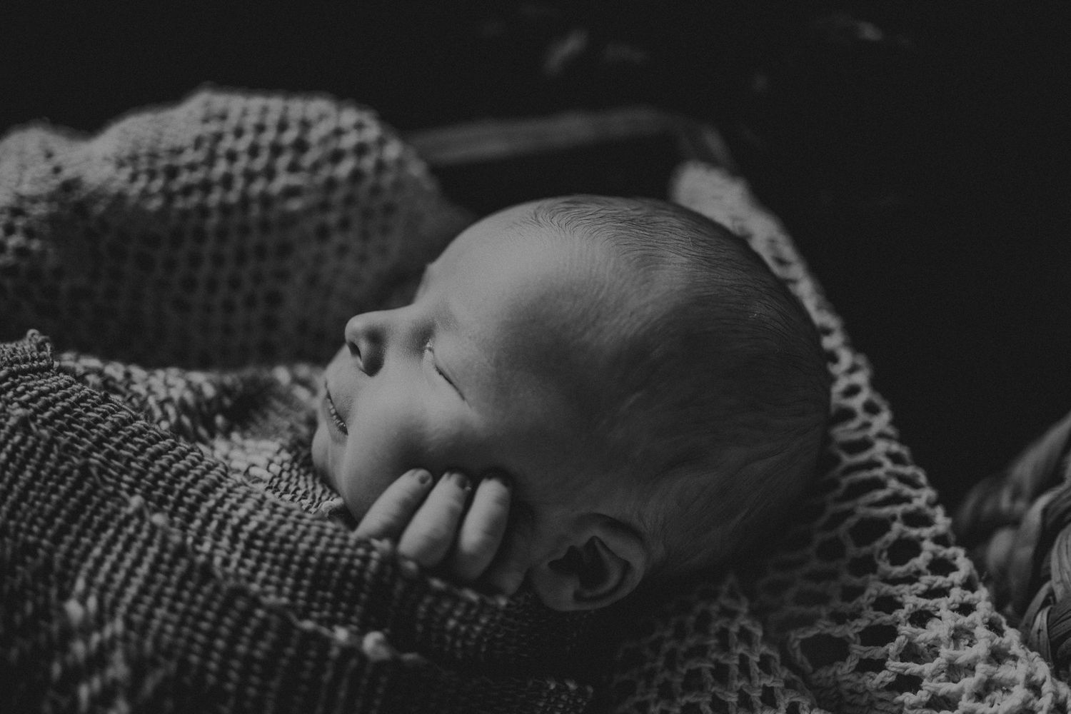 Black and white portrait of sleeping infant on knitted blanket.