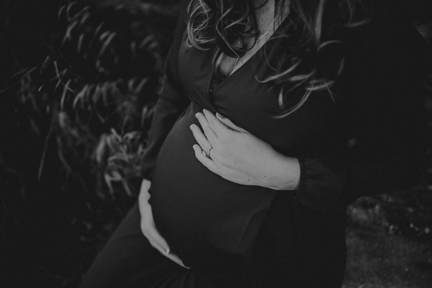 A black and white close-up of an expectant mother cradling her baby bump.
