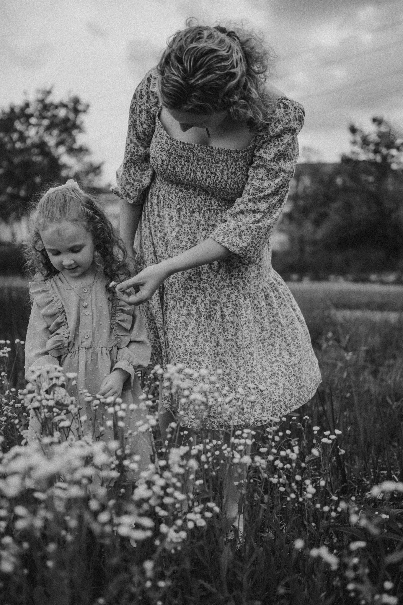 Mother and child explore wildflowers together in a dreamy black and white meadow scene.