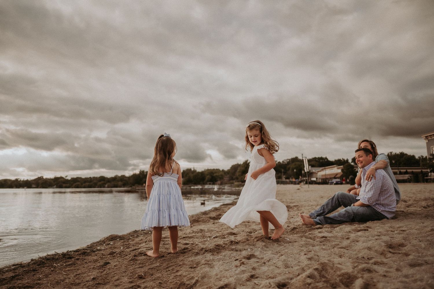 A playful beach scene with people sitting and dancing in the sand at sunset.