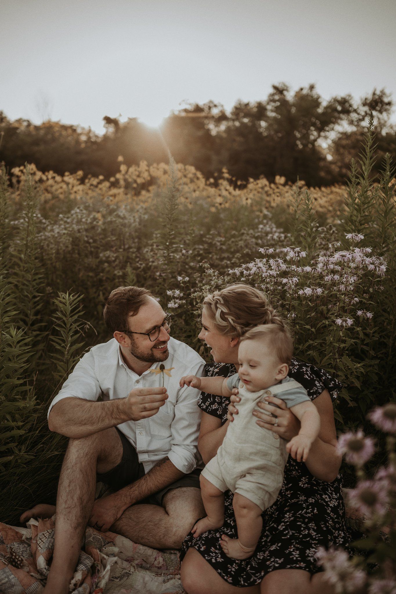 Family shares intimate moment while sitting in wildflower meadow during golden hour.