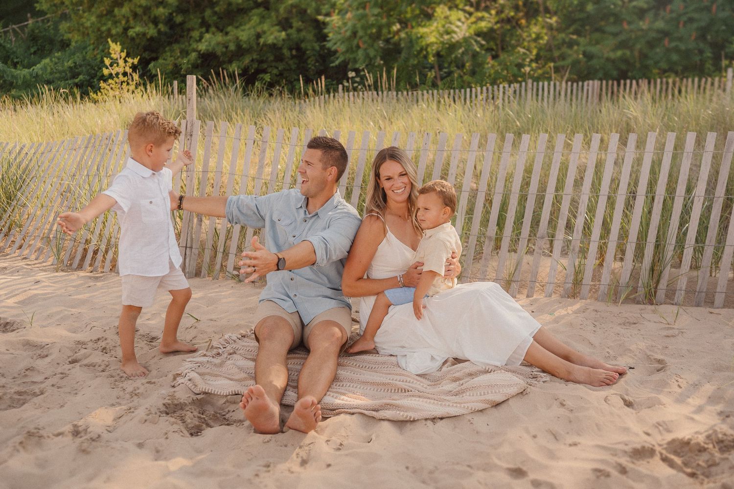 Casual beach photoshoot with sandy shore and wooden fence at sunset.