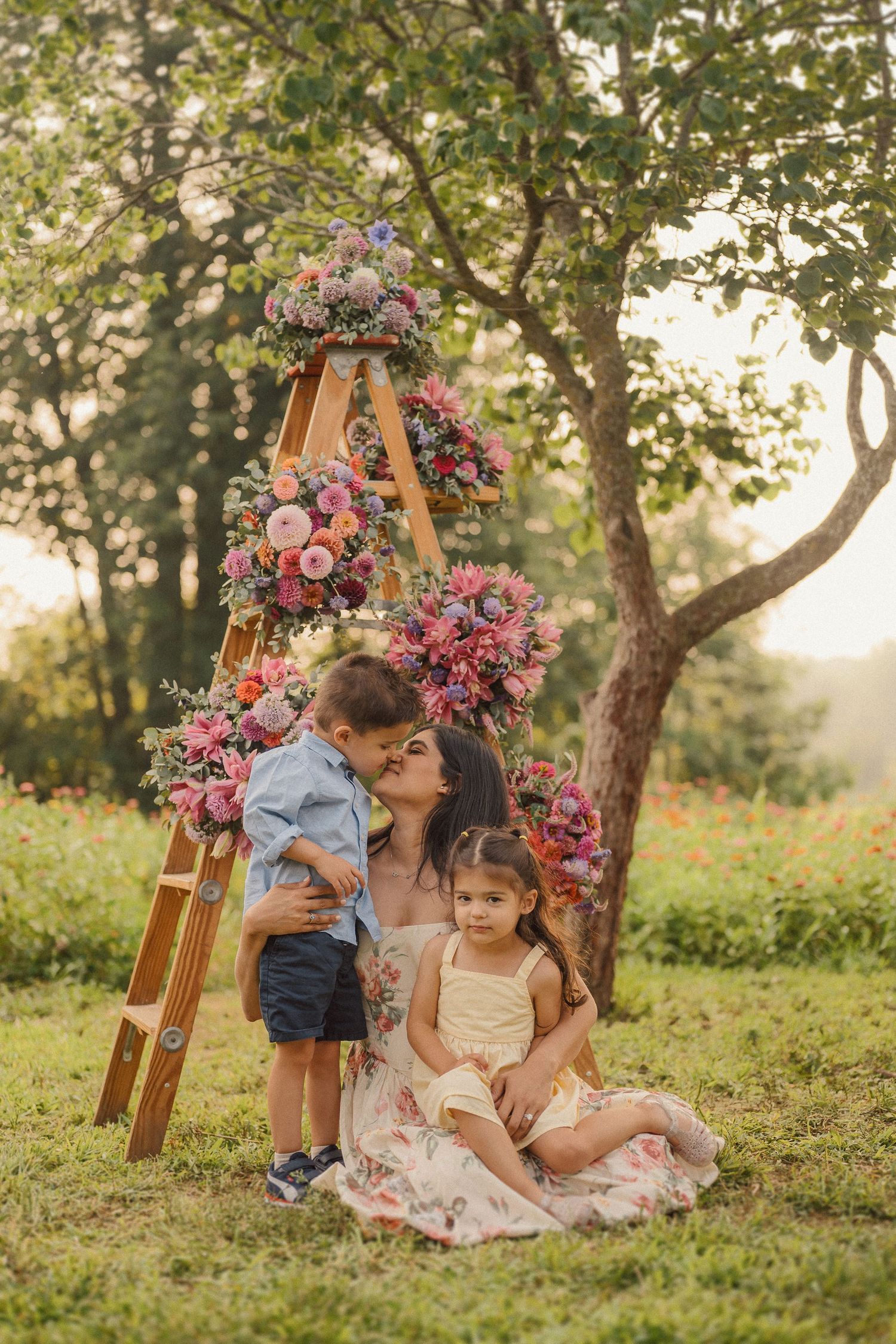 A tender family moment captured outdoors with a decorated ladder and floral arrangements in the background.