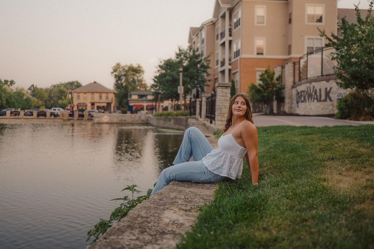 Casual portrait by waterfront with urban architecture in background at dusk.