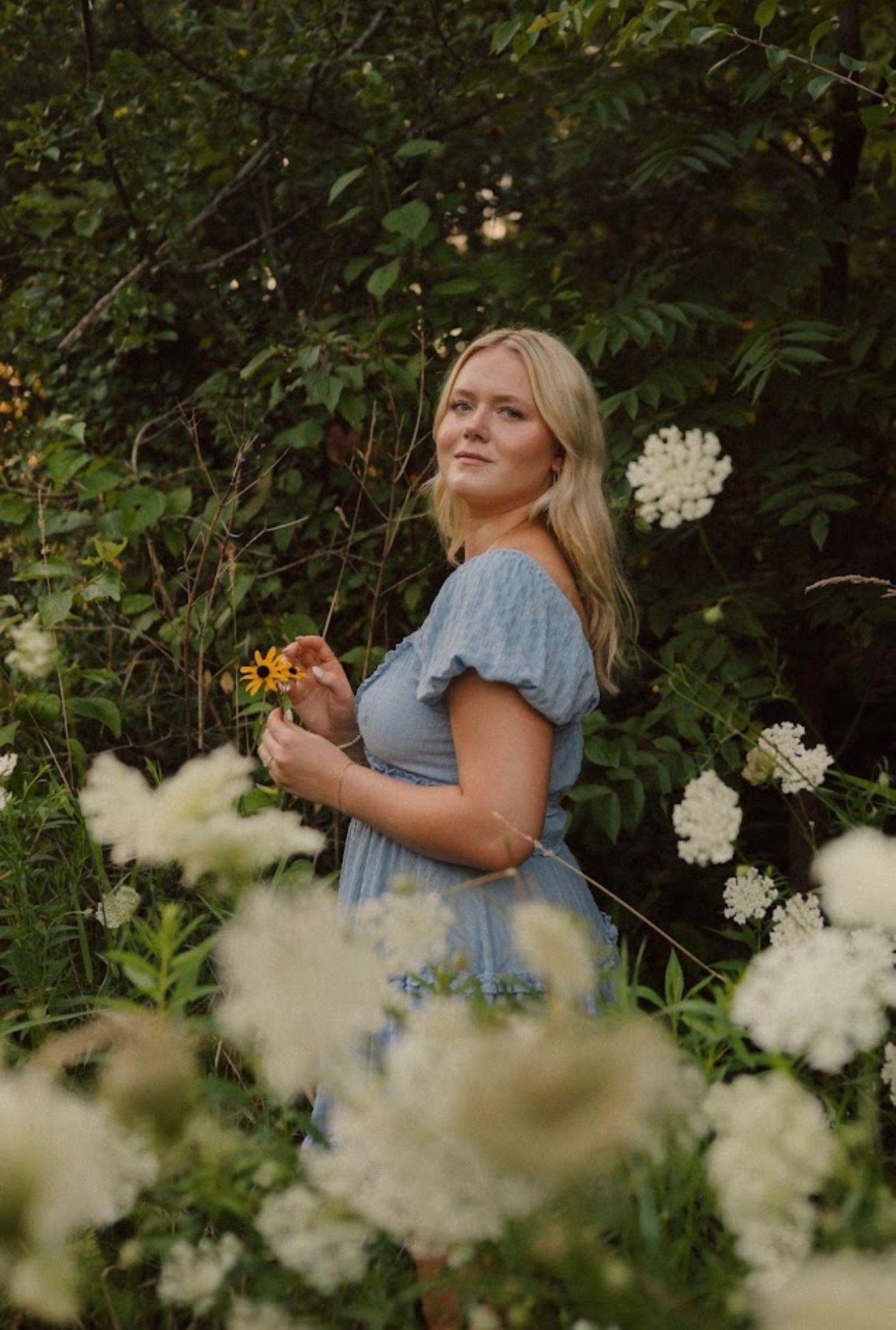 Blue dress among white wildflowers in lush garden setting.
