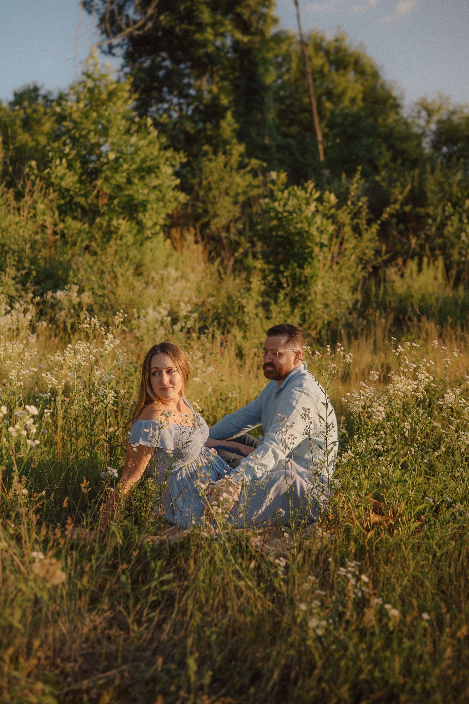 A couple sits together in a wildflower meadow during golden hour.