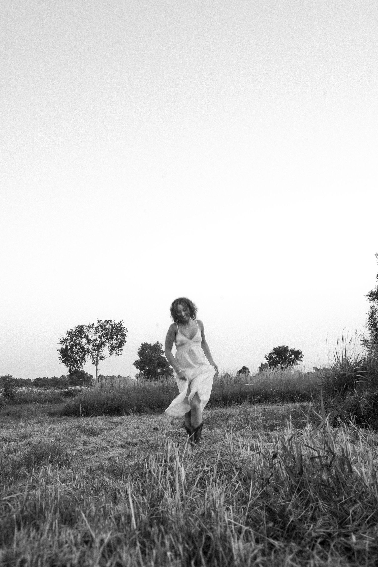 Black and white image of someone dancing in a rural field with tall grass at dusk.