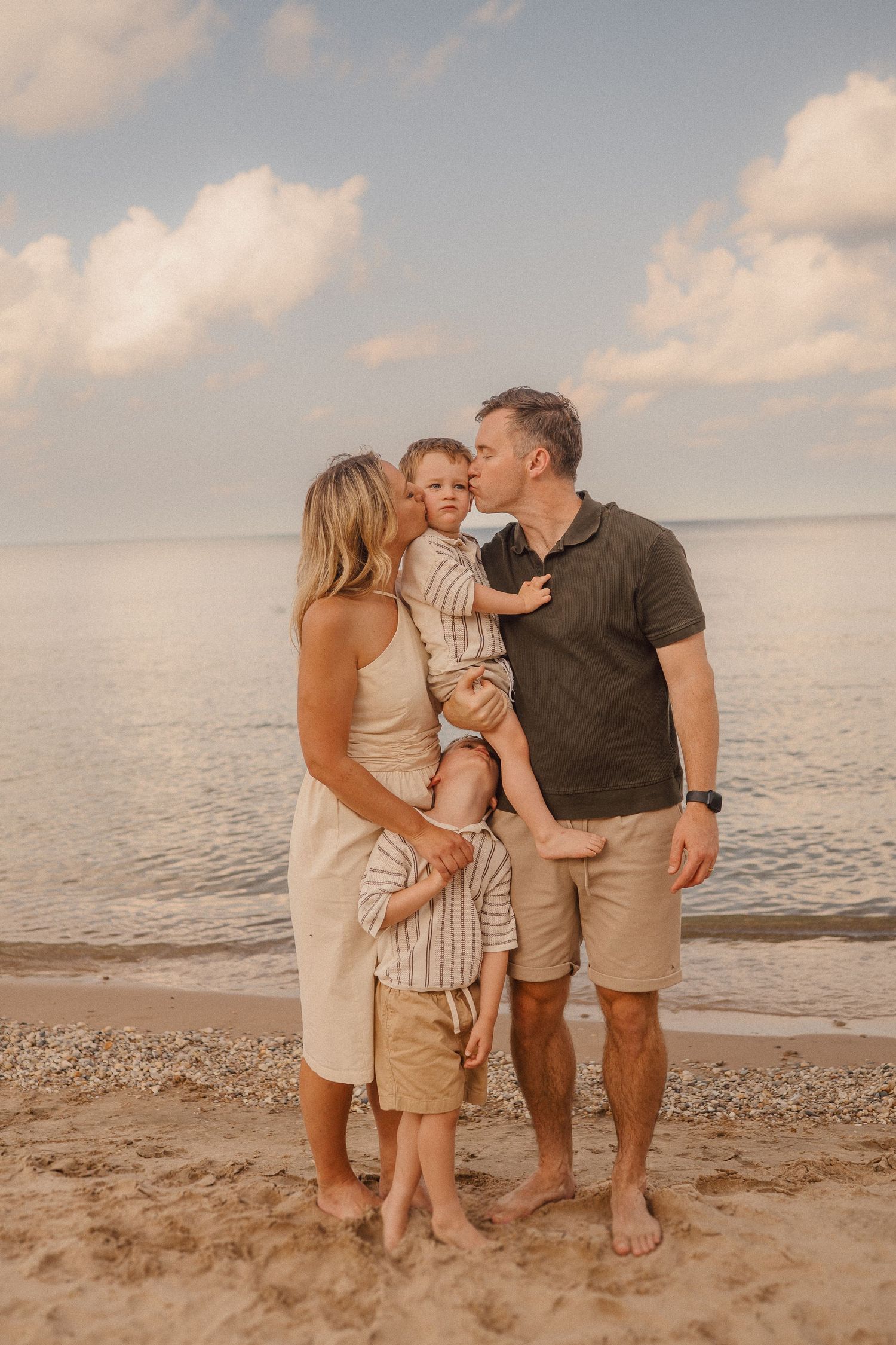 A family enjoys a tender moment together on a sandy beach at sunset with calm waters in the background.