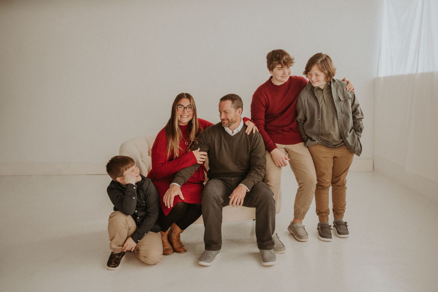 Family posed on white studio floor wearing coordinated casual outfits in burgundy and brown.