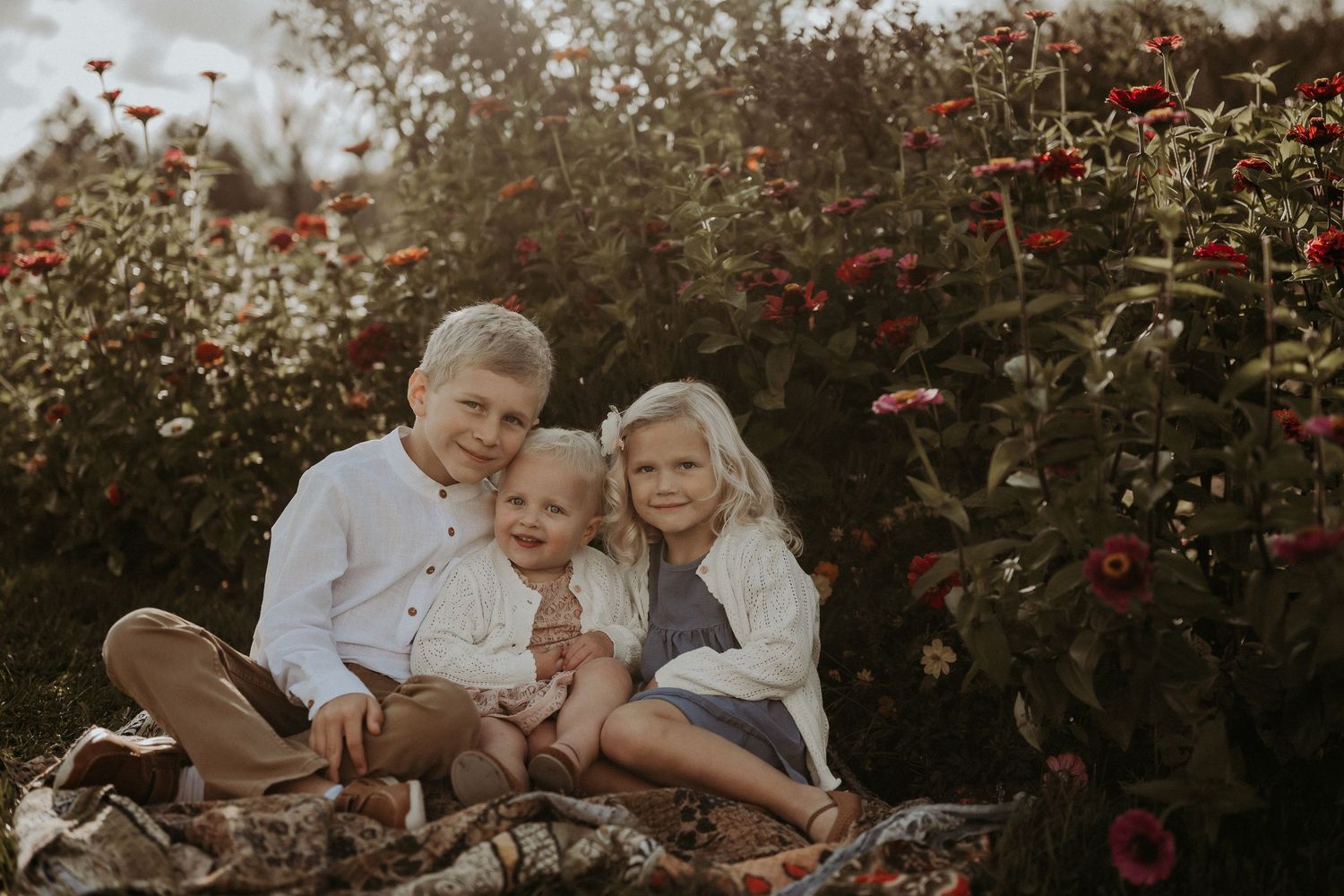 Three people sitting together among blooming red flowers at sunset.