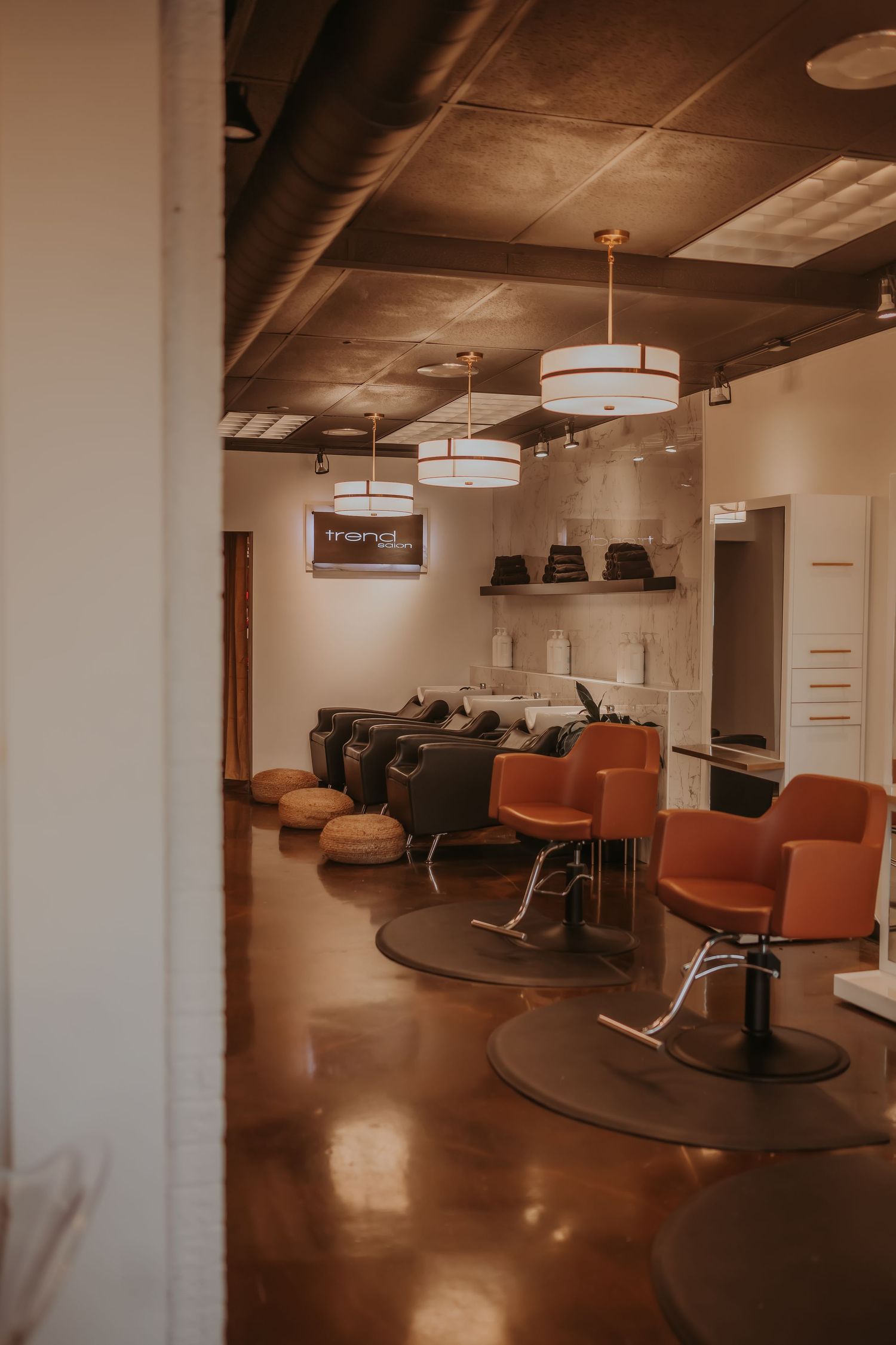Modern salon interior with orange styling chairs and drum pendant lighting creating a warm, inviting atmosphere.