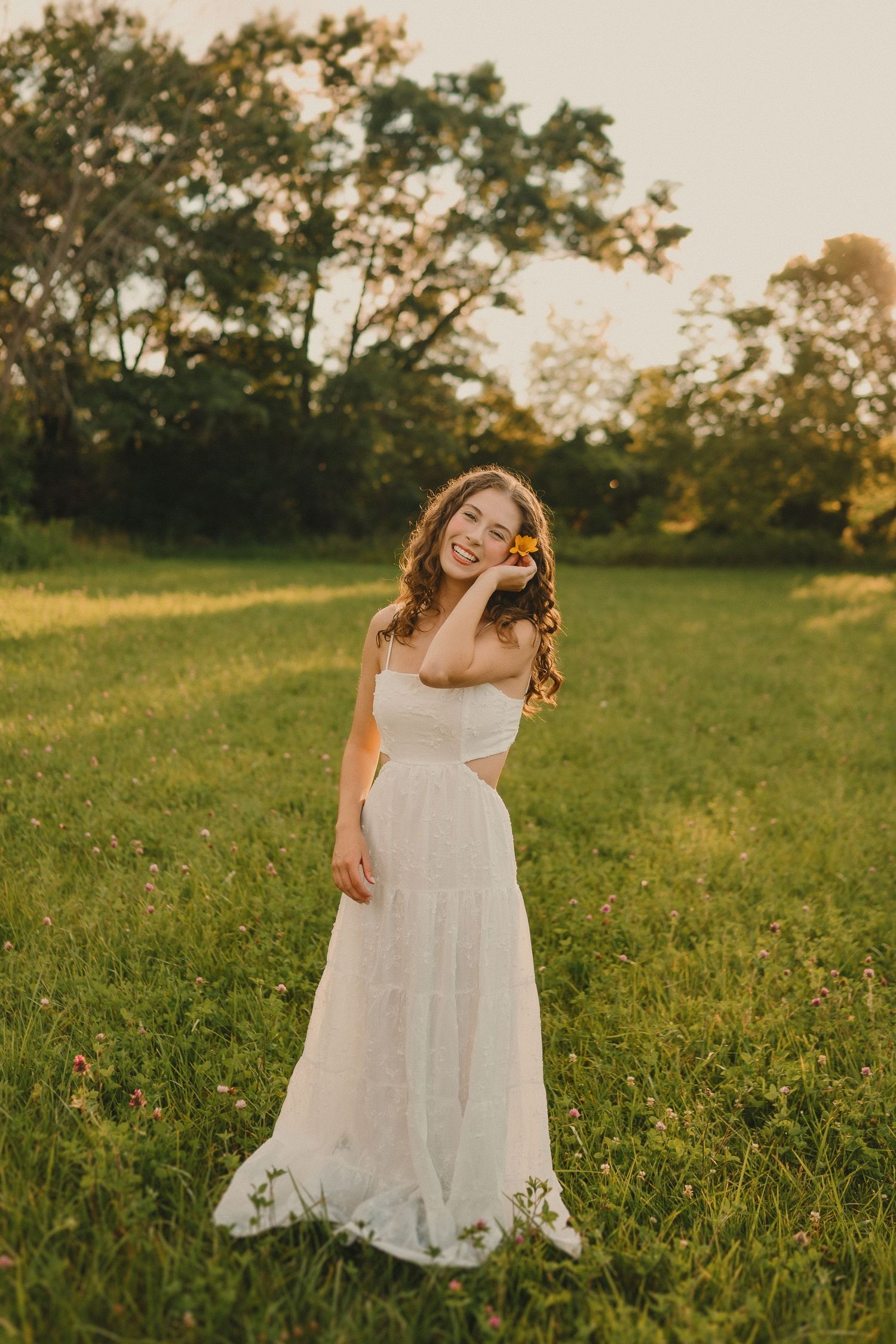 A dreamy full-length portrait shows someone twirling in a white dress in a sunlit meadow.