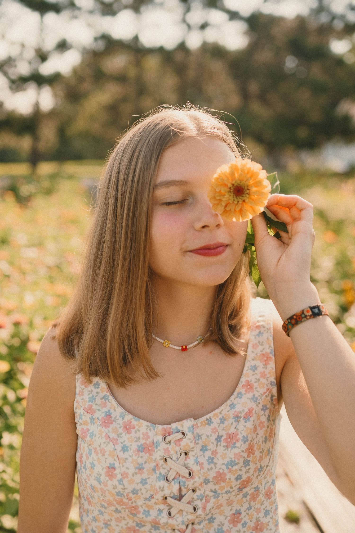 A dreamy summer portrait with a person holding a golden dandelion flower in front of their eye in warm sunlight.