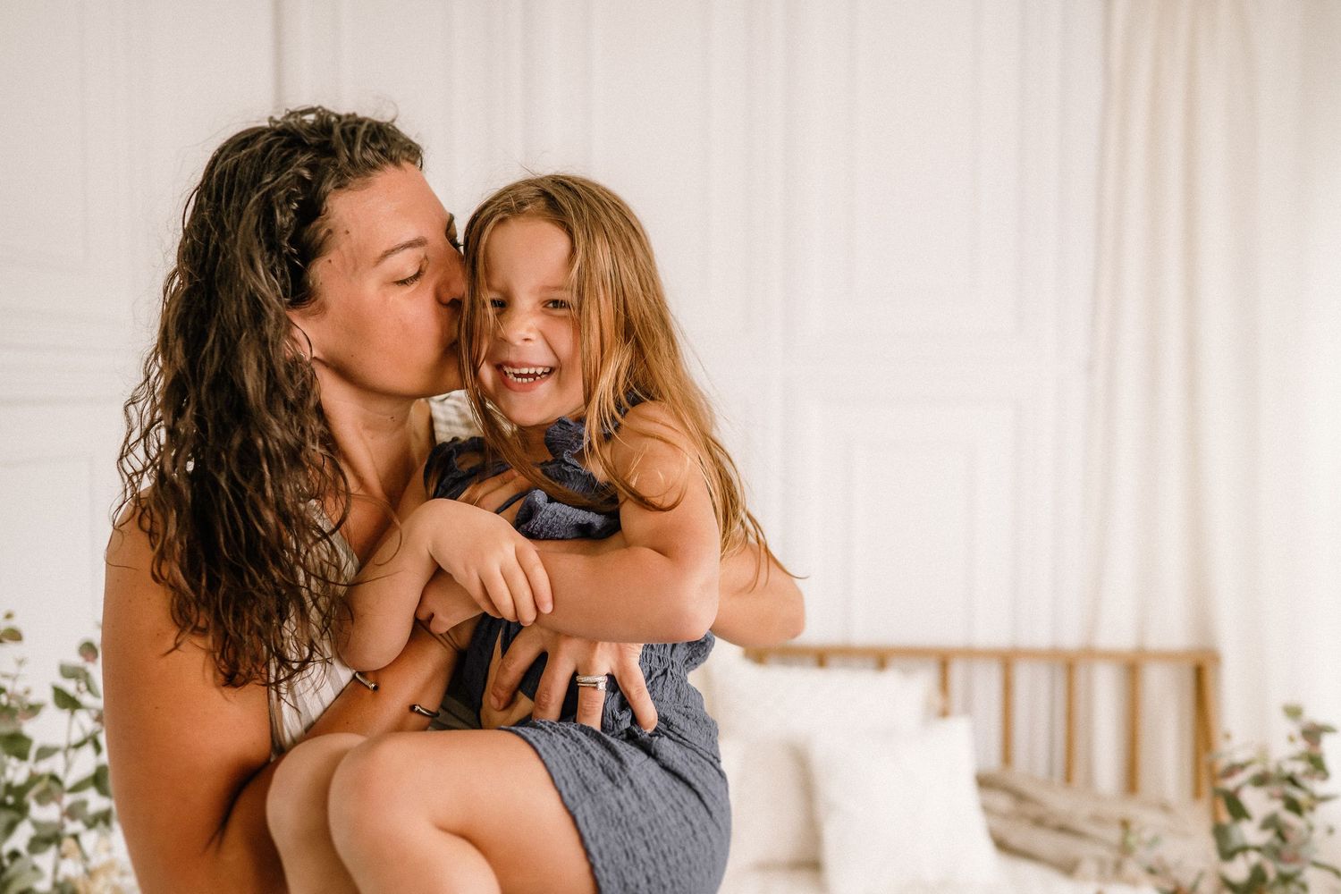 A tender family moment captured indoors with warm lighting and white curtains in the background.