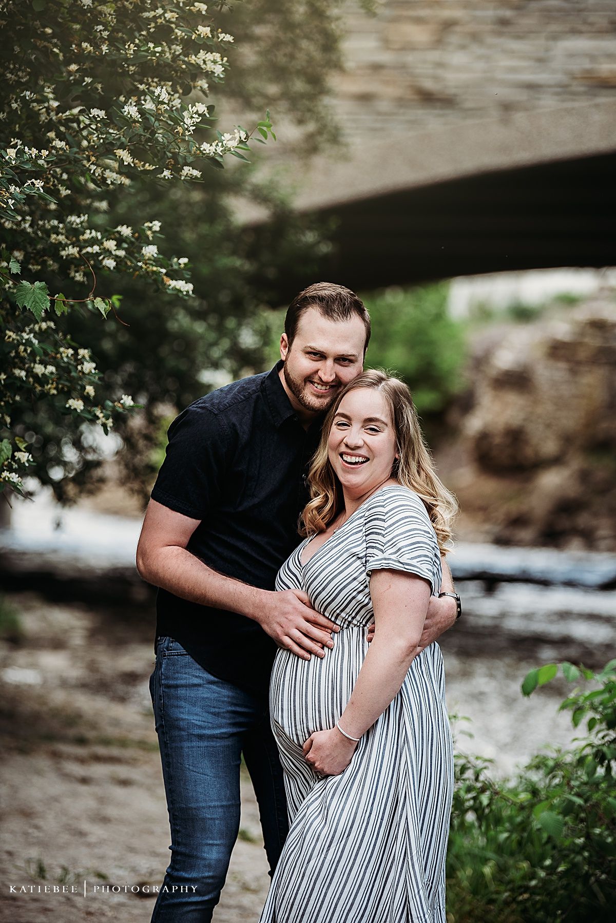 Expecting couple sharing a laugh together by a stone bridge.
