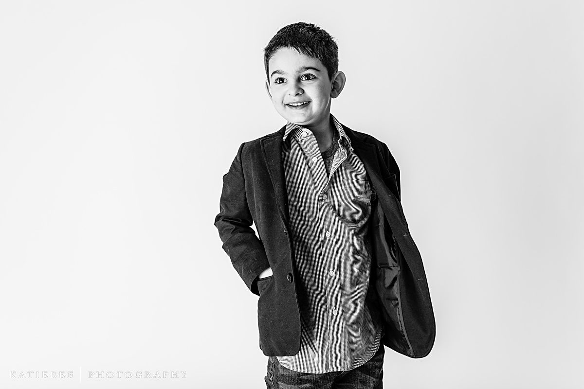 Black and white studio shot of child in blazer and striped shirt with hands in pockets.