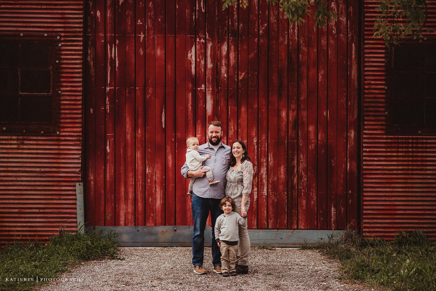 Family poses together in front of large red barn during outdoor photo session.