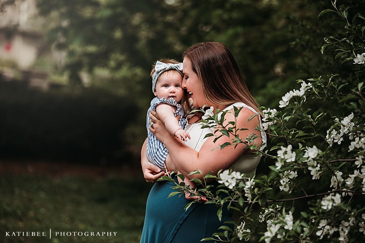 Sweet outdoor portrait amongst white flowering bushes with baby in striped outfit.