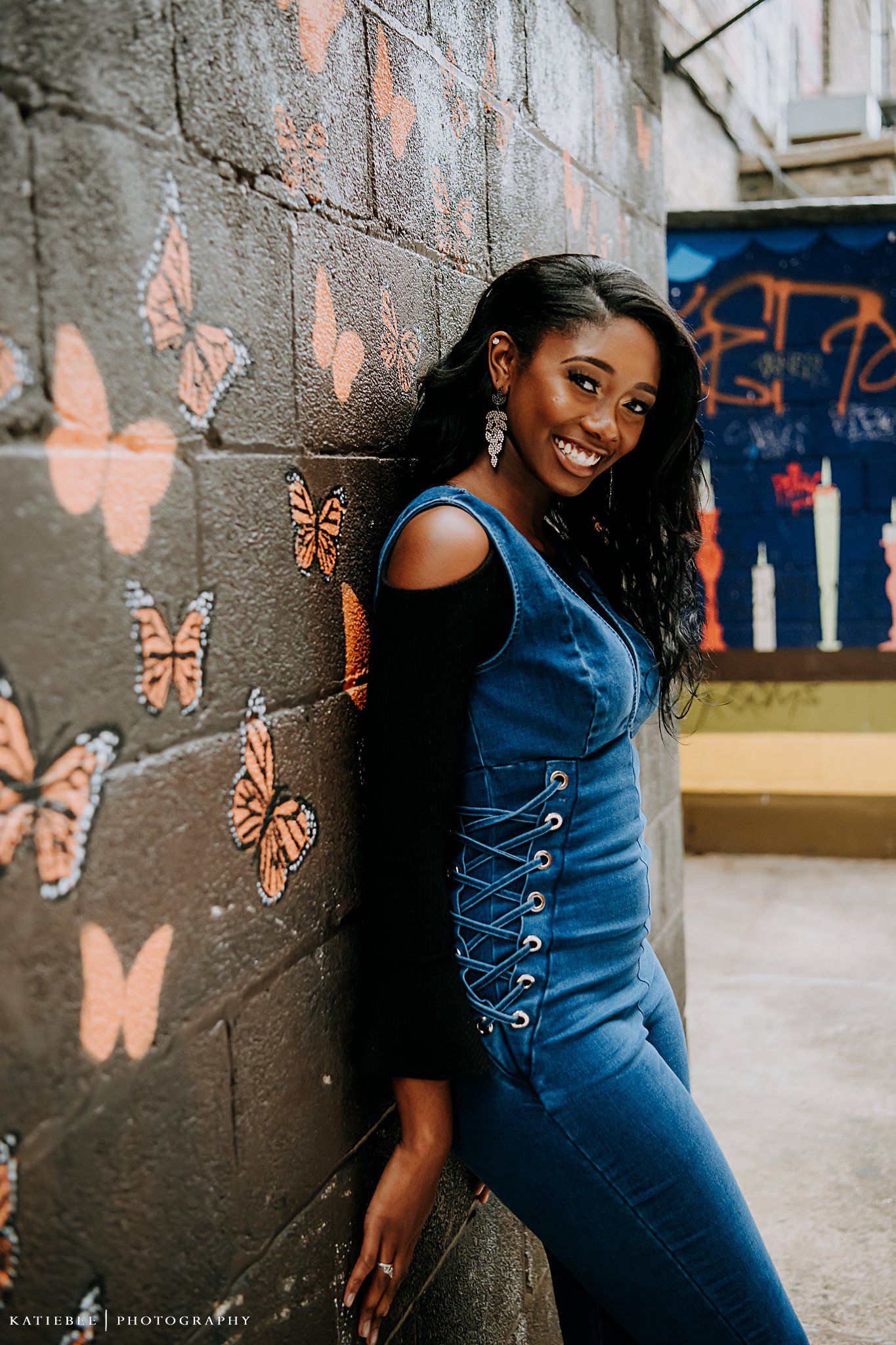 Portrait against a dark wall with painted orange butterflies in an outdoor urban setting.