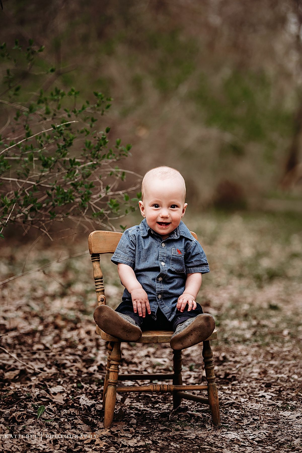 Smiling baby in blue shirt sitting on vintage wooden chair surrounded by nature.