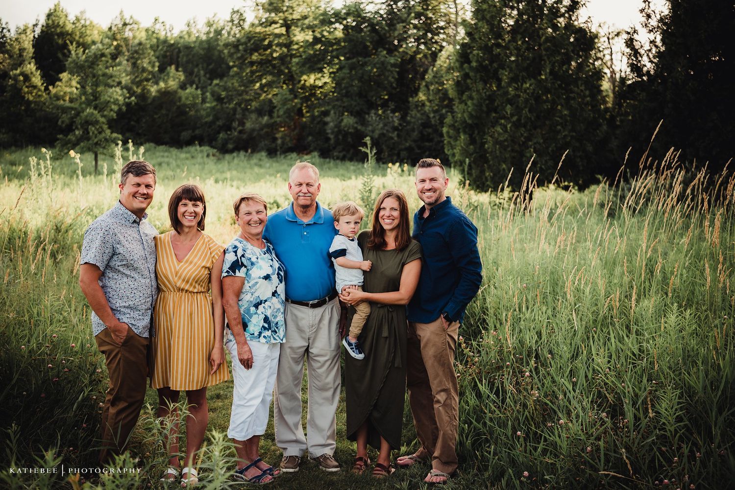 A multigenerational family portrait in casual attire against a background of summer meadow grass.