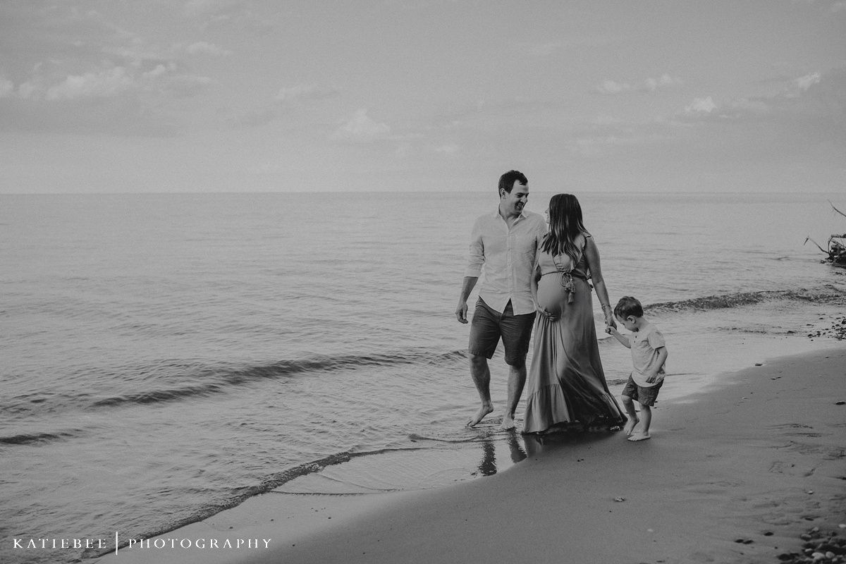 Black and white beach photo of family walking together along ocean shore.