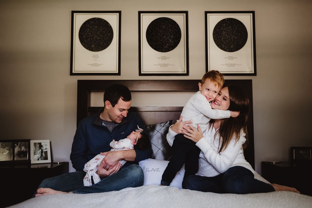 Intimate family moment captured on bed with circular art pieces hanging above headboard.