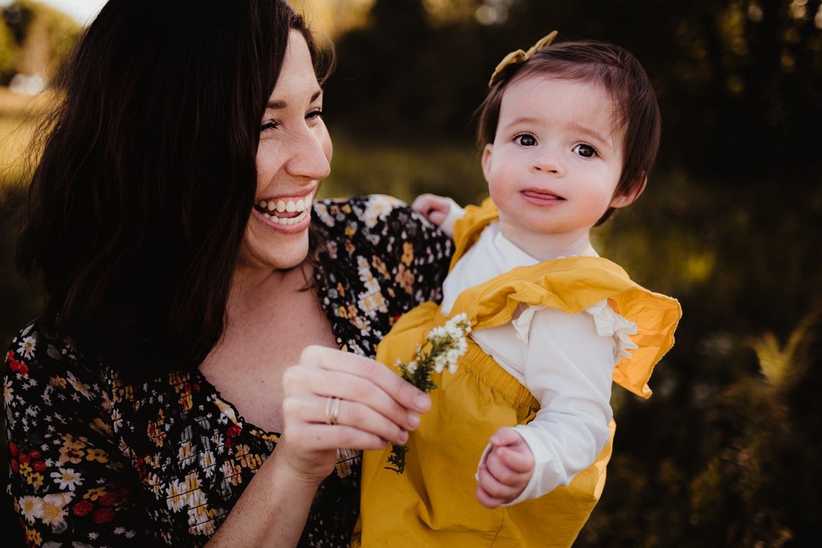 Candid outdoor shot of adult in floral print holding happy baby wearing yellow and white.