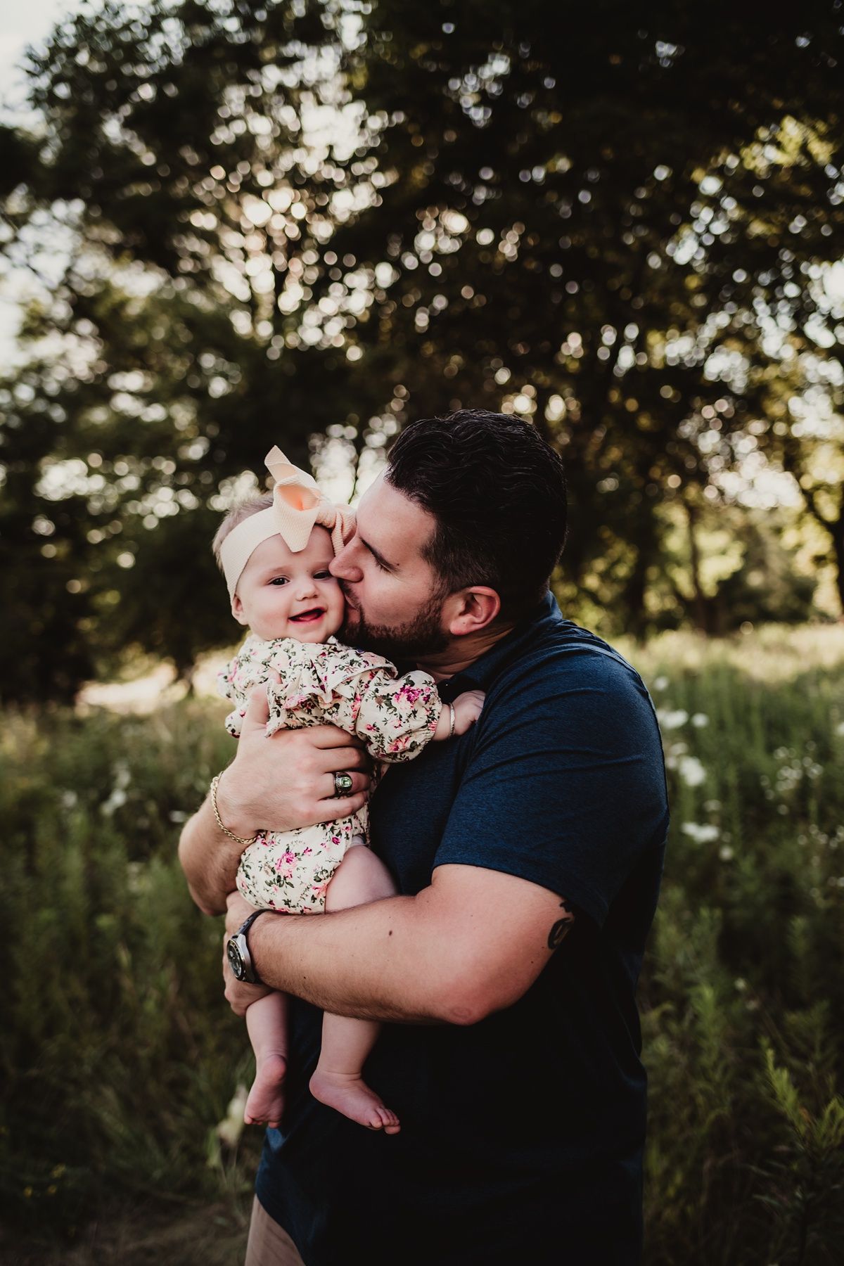 Tender moment between parent and baby in floral outfit against sunset backdrop.